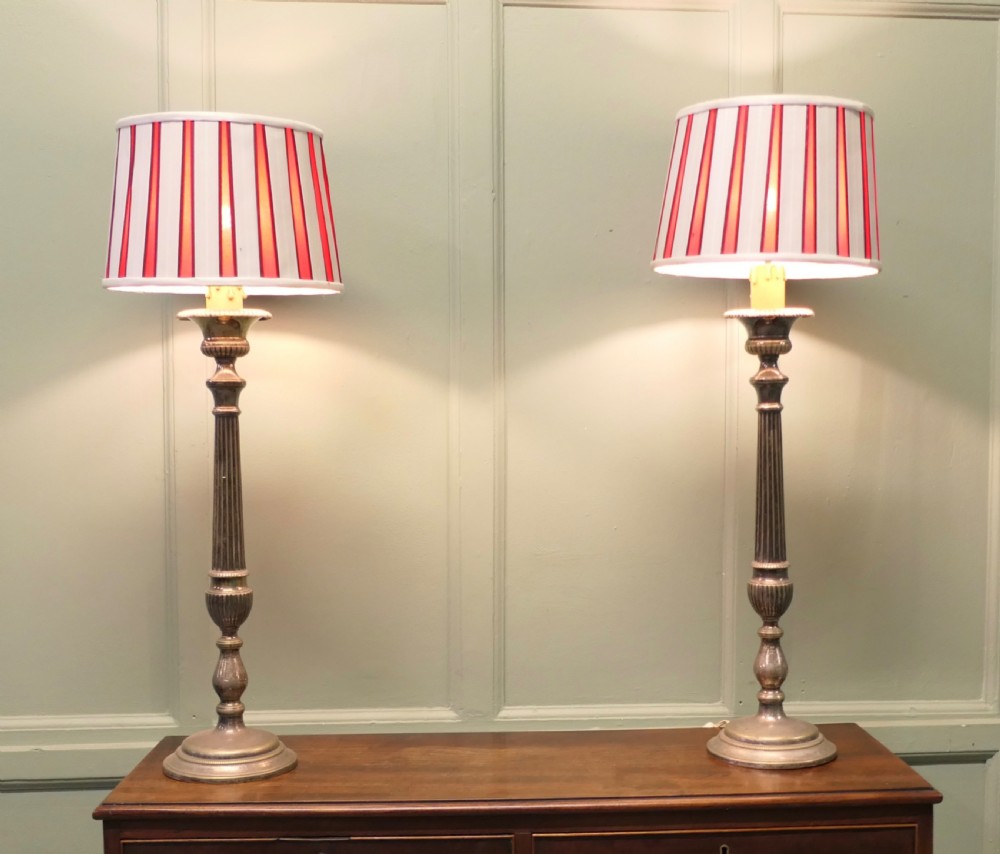 A pair of tall silver plated candlestick table lamps featuring reeded column stems and red and white striped shades.