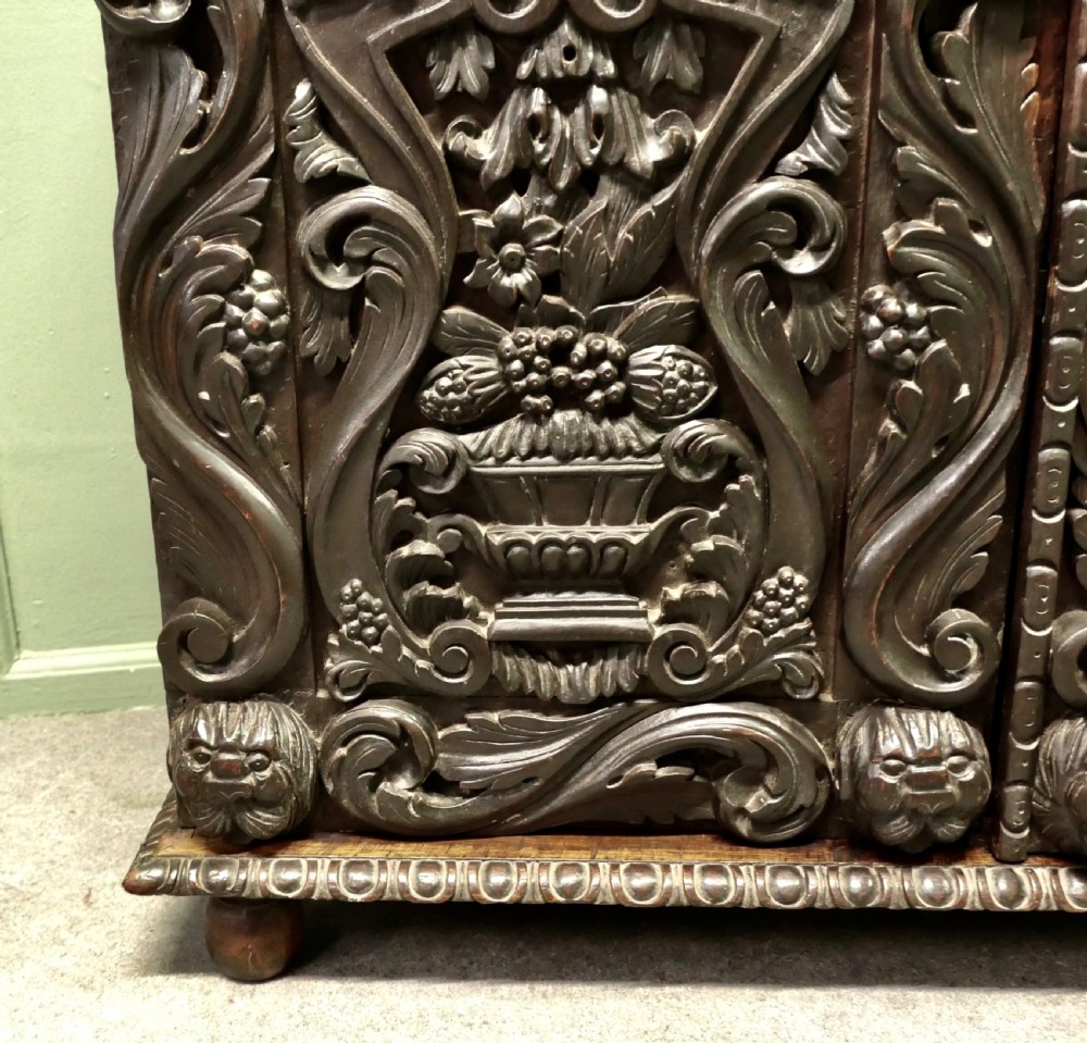 A dark brown oak cupboard featuring two doors adorned with detailed foliate and mask relief carvings. View III