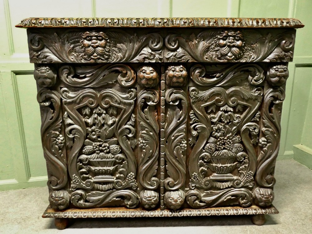 A dark brown oak cupboard featuring two doors adorned with detailed foliate and mask relief carvings. View IV