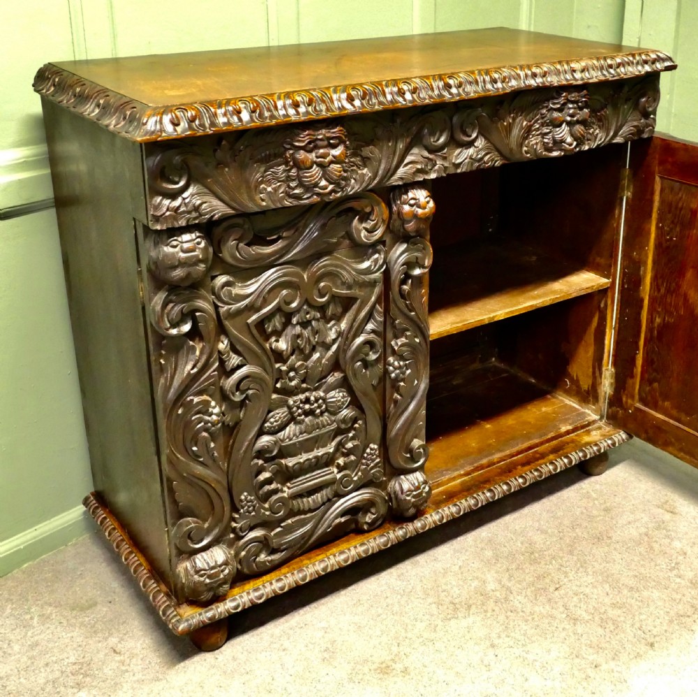 A dark brown oak cupboard featuring two doors adorned with detailed foliate and mask relief carvings. View V