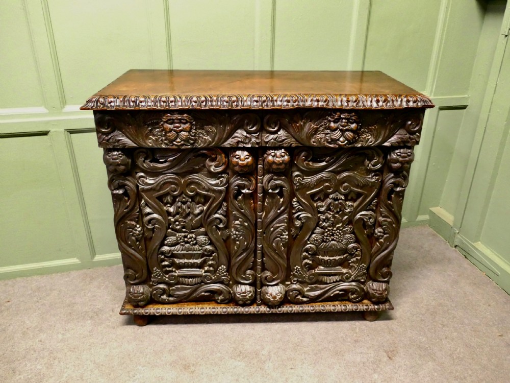 A dark brown oak cupboard featuring two doors adorned with detailed foliate and mask relief carvings. View VI
