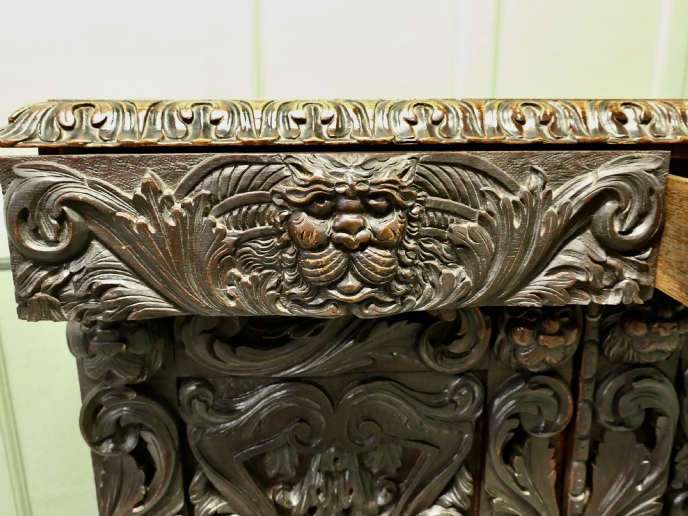 A dark brown oak cupboard featuring two doors adorned with detailed foliate and mask relief carvings. View VII