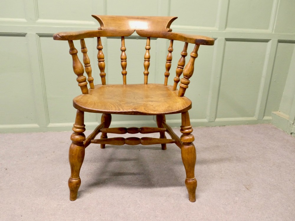 A 19th-century smokers bow armchair made from beech and elm with turned spindles and a contoured saddle seat.