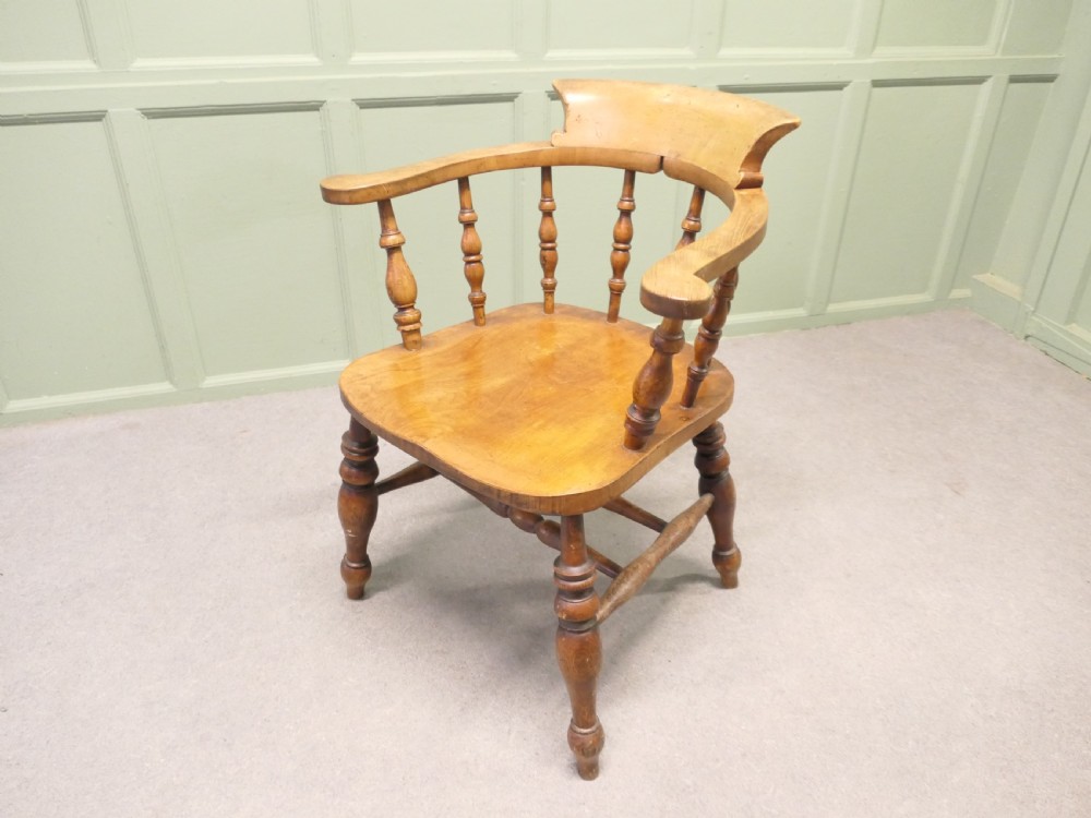 A 19th-century wooden smokers bow desk chair crafted from beech and elm with turned spindles and a shaped saddle seat.