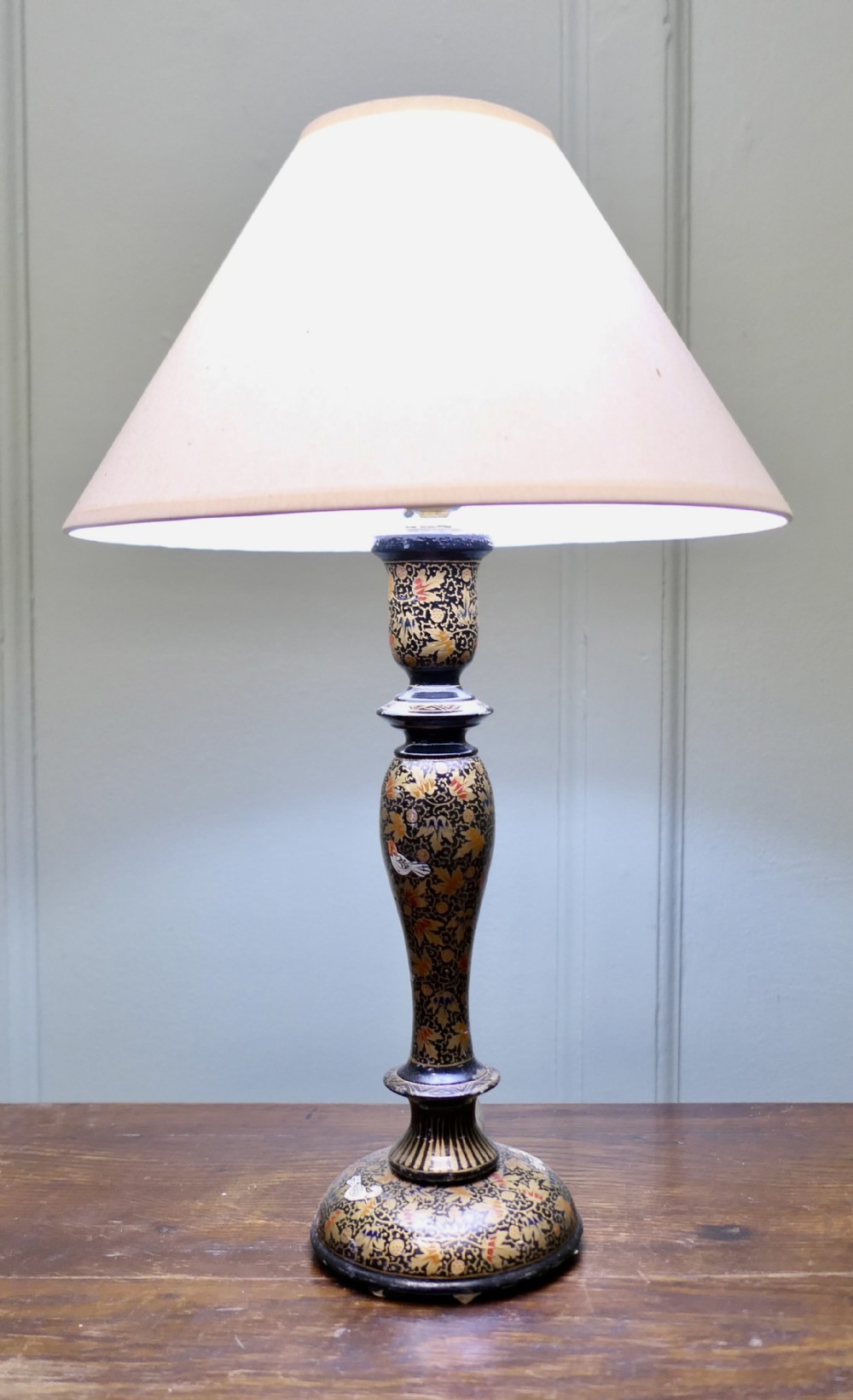 A hand-painted turned table lamp base featuring detailed gold floral motifs and bird illustrations, topped with a cream conical shade.