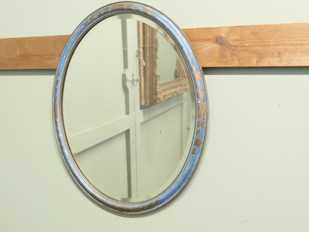 An Art Deco oval wall mirror featuring a pale blue painted frame with carved gilt leaf motifs enclosing an oval glass mirror plate.