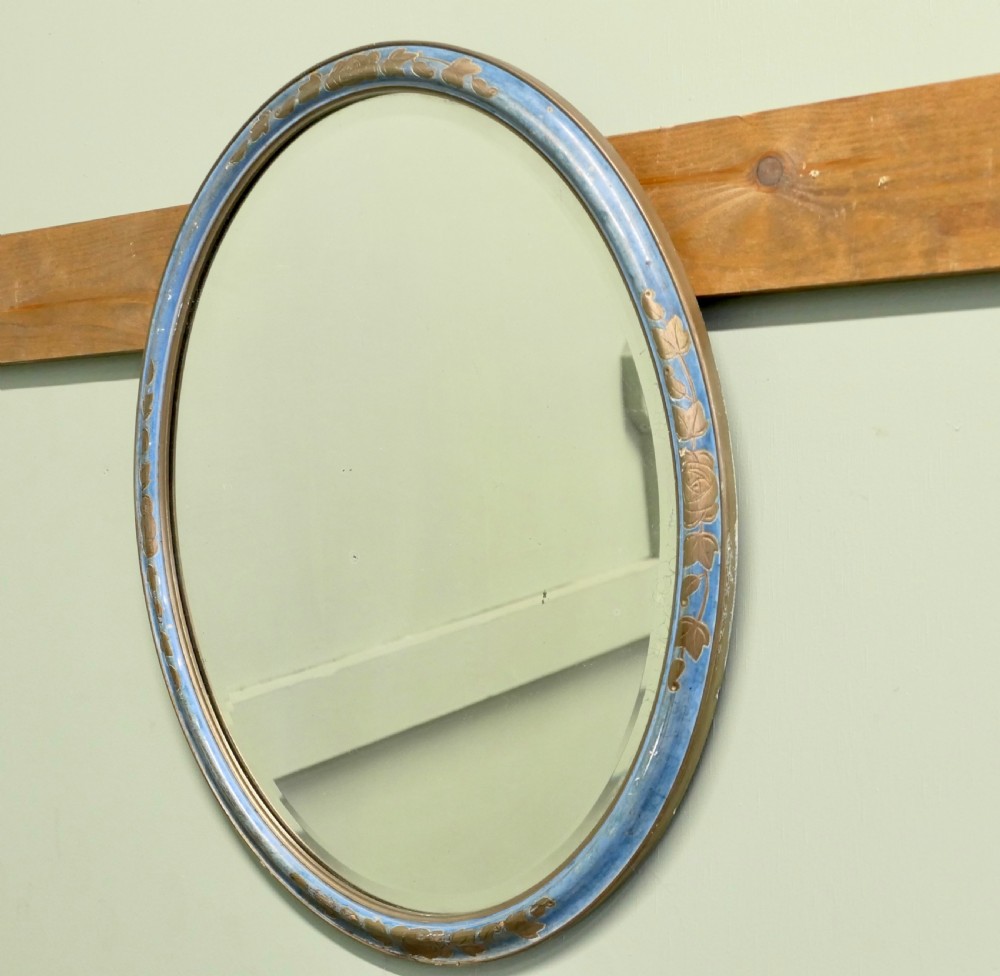 An Art Deco oval wall mirror featuring a pale blue painted frame with carved gilt leaf motifs enclosing an oval glass mirror plate. View II