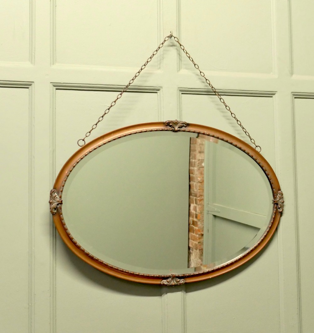 An oval copper-framed wall mirror featuring decorative acanthus leaf mounts at four points and a beaded inner border, suspended by a metal chain. View III