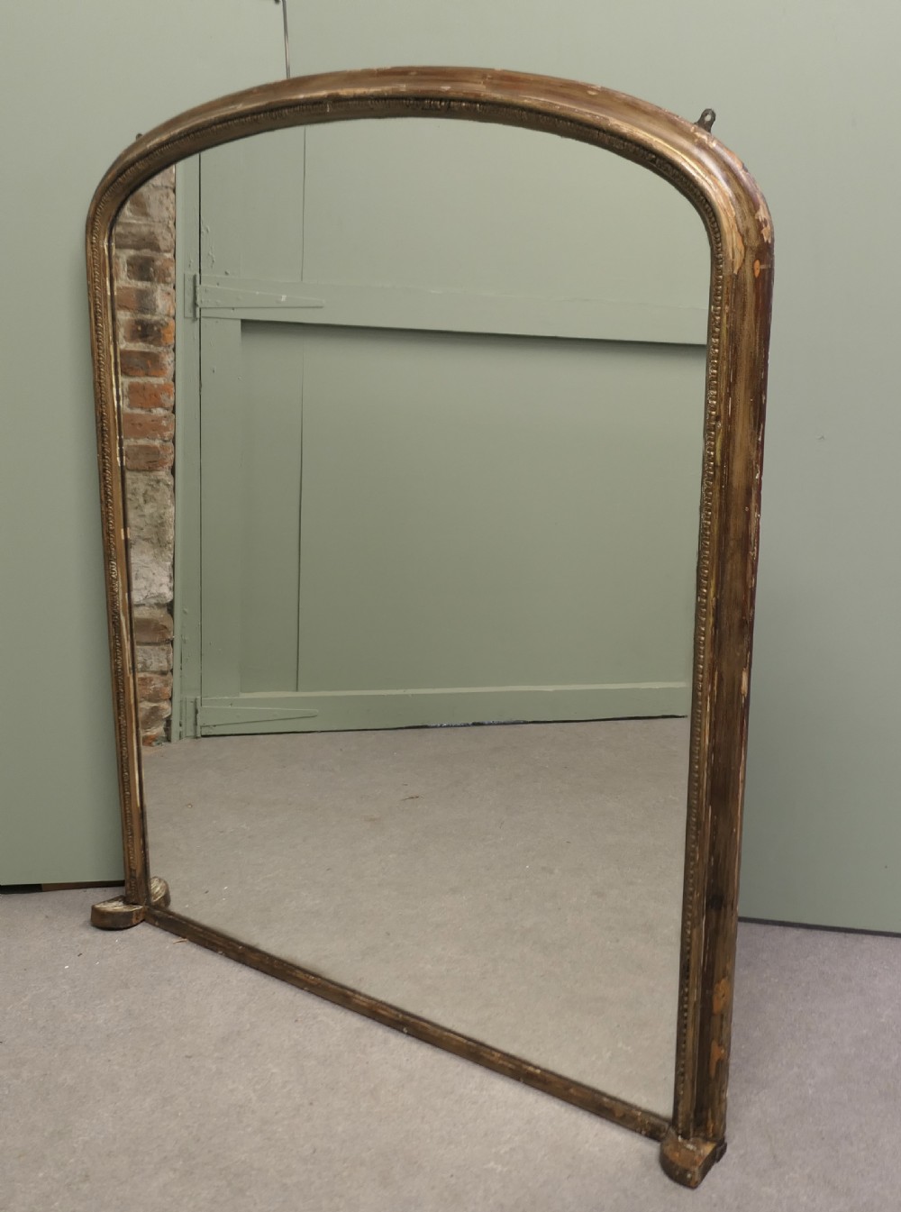 A large Victorian arched overmantel mirror featuring a distressed giltwood frame with subtle beaded moulding and a flat base.