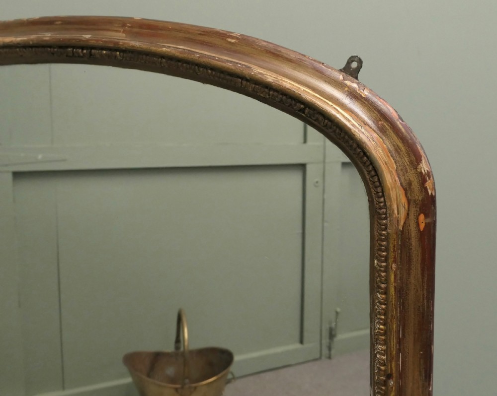 A large Victorian arched overmantel mirror featuring a distressed giltwood frame with subtle beaded moulding and a flat base. View II
