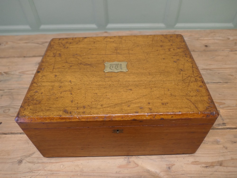 A rectangular warm brown Victorian oak presentation box featuring a hinged lid with a central brass monogrammed plaque and a keyhole on the front face.