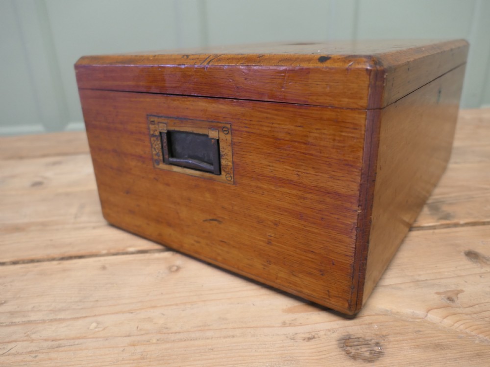 A rectangular warm brown Victorian oak presentation box featuring a hinged lid with a central brass monogrammed plaque and a keyhole on the front face. View IV