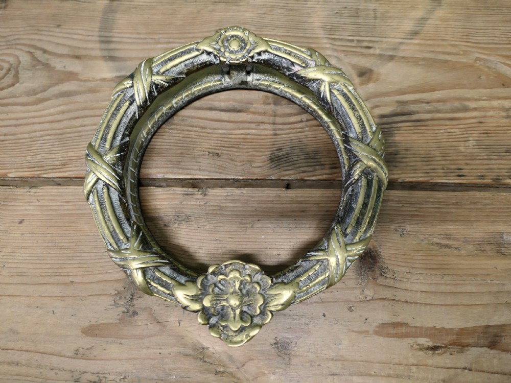 An aged cast brass ring door knocker featuring a floral rosette motif and a textured circular ring. View II