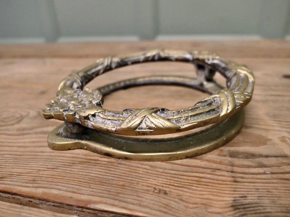 An aged cast brass ring door knocker featuring a floral rosette motif and a textured circular ring. View IV