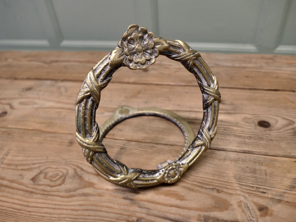 An aged cast brass ring door knocker featuring a floral rosette motif and a textured circular ring. View VI