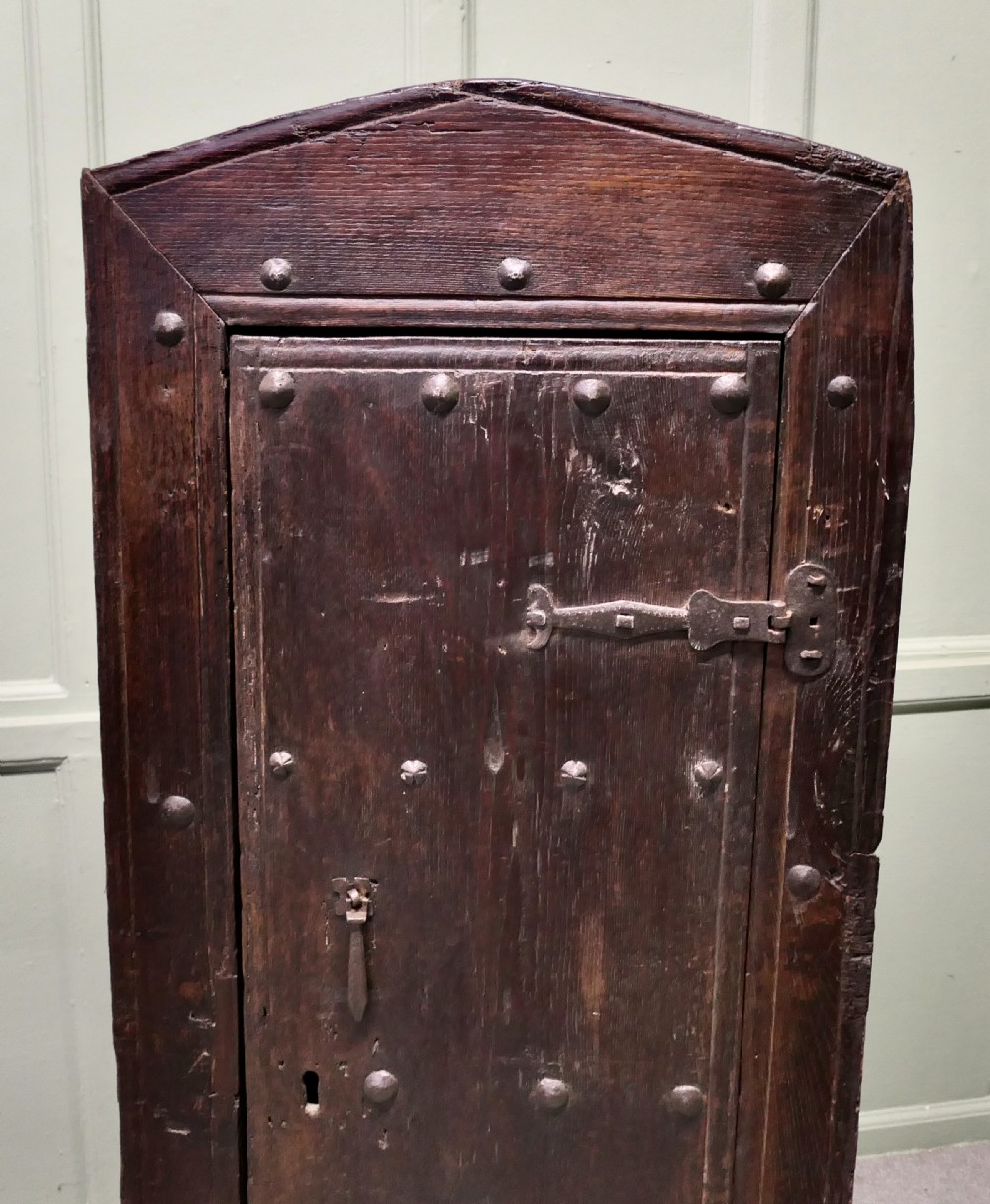 A narrow dark oak alcove cupboard featuring an arched top frame, iron studs, and hand-forged wrought iron hinges. View III