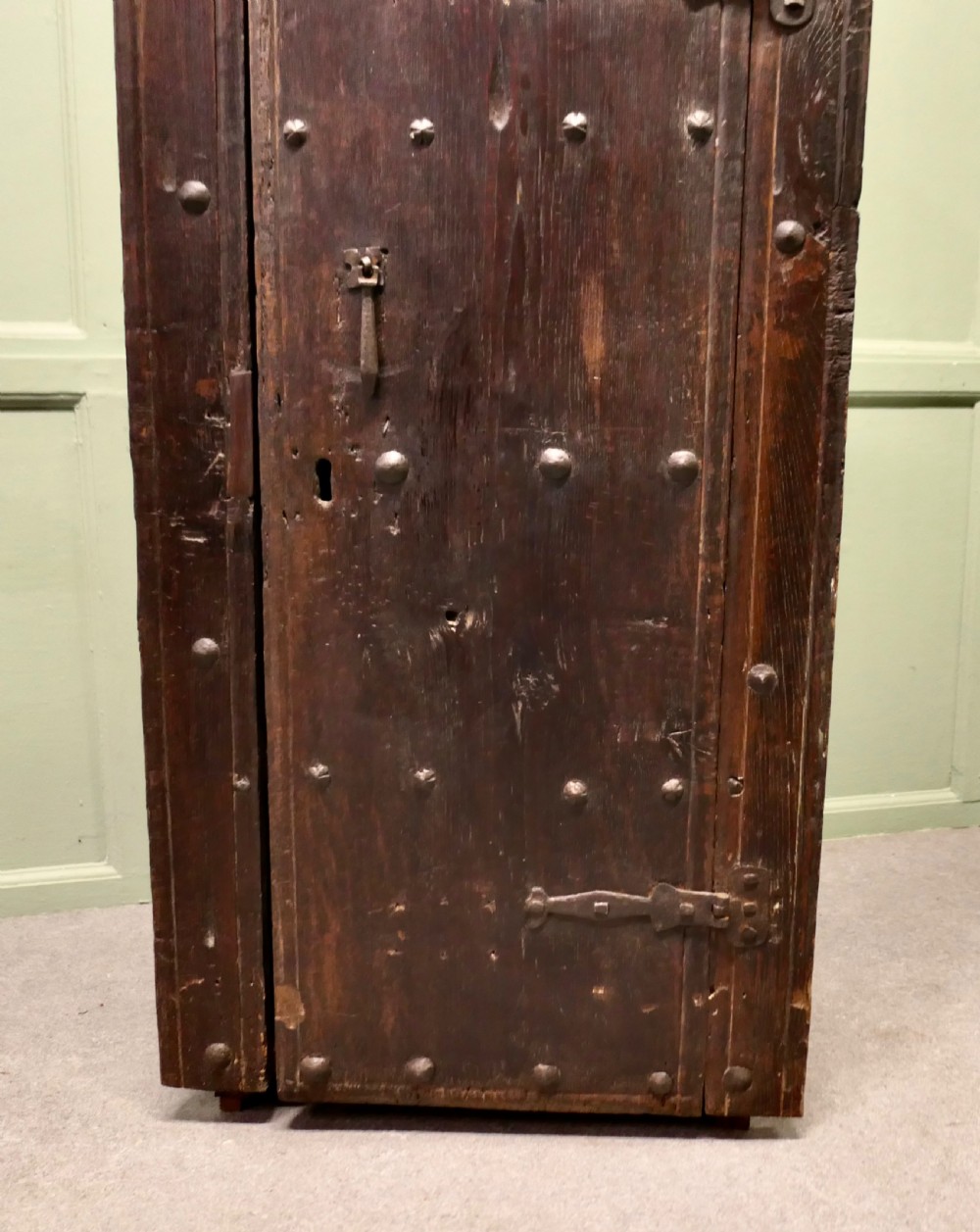 A narrow dark oak alcove cupboard featuring an arched top frame, iron studs, and hand-forged wrought iron hinges. View IV