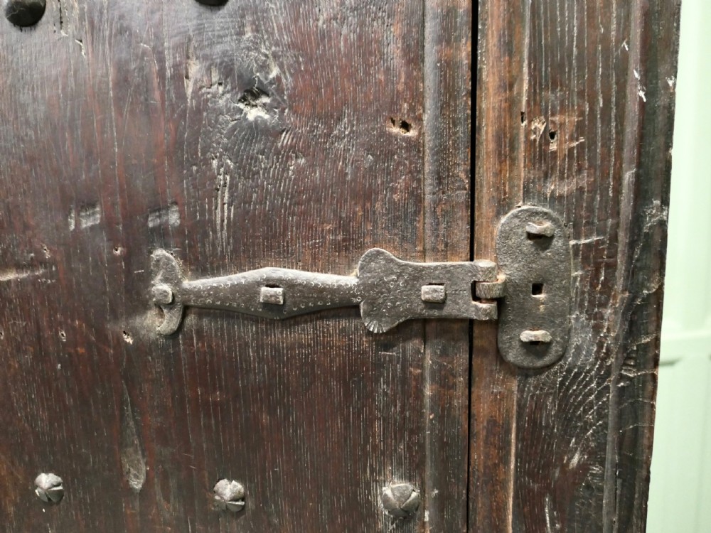 A narrow dark oak alcove cupboard featuring an arched top frame, iron studs, and hand-forged wrought iron hinges. View VII