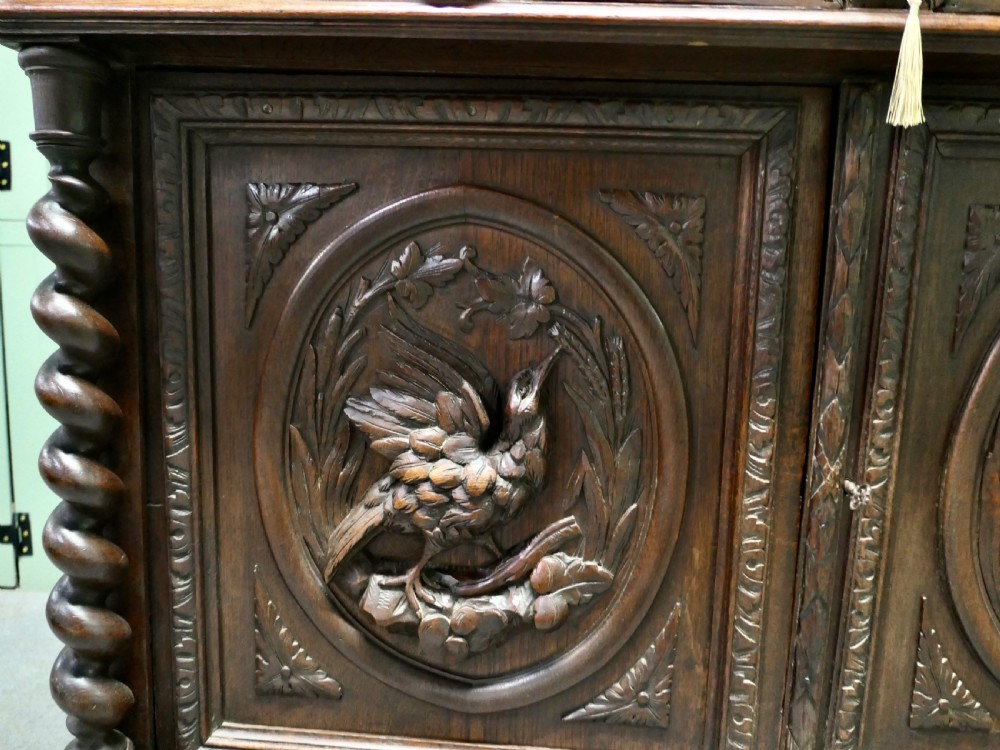 A dark brown carved oak French sideboard featuring two frieze drawers above twin cupboard doors with oval medallions depicting relief-carved game birds, flanked by barley twist columns. View II