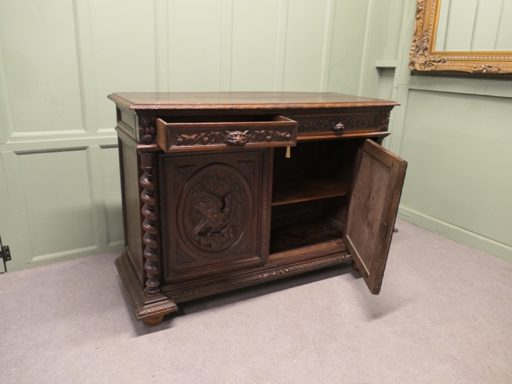 A dark brown carved oak French sideboard featuring two frieze drawers above twin cupboard doors with oval medallions depicting relief-carved game birds, flanked by barley twist columns. View III