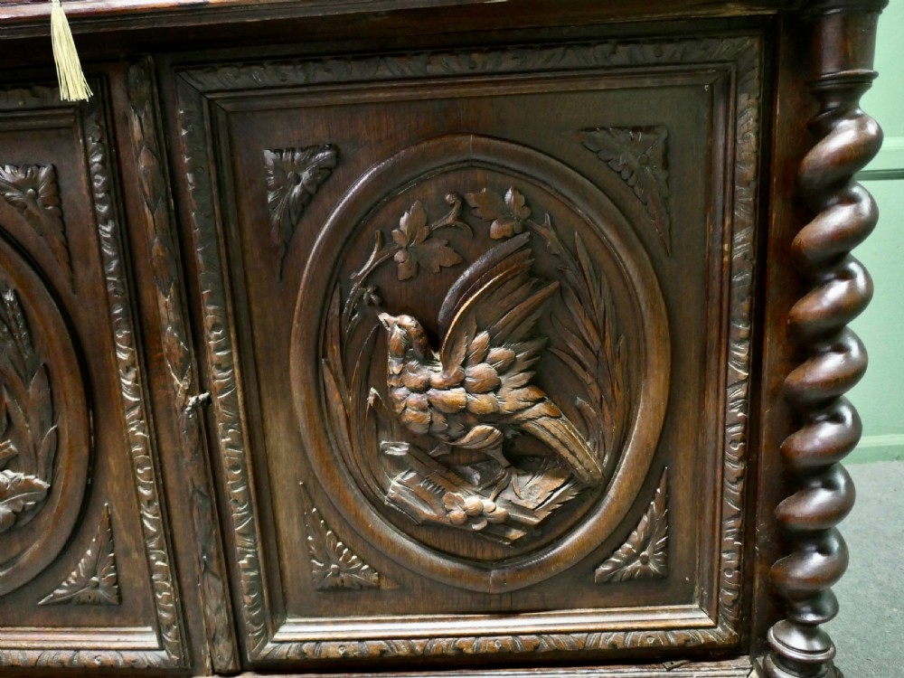 A dark brown carved oak French sideboard featuring two frieze drawers above twin cupboard doors with oval medallions depicting relief-carved game birds, flanked by barley twist columns. View IV