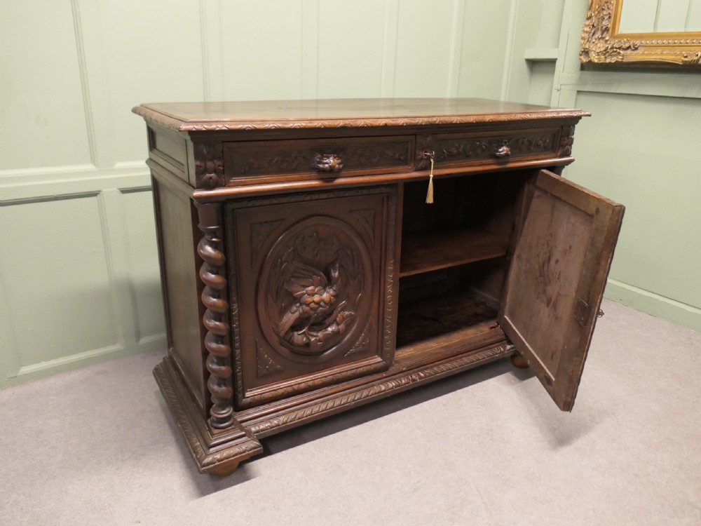 A dark brown carved oak French sideboard featuring two frieze drawers above twin cupboard doors with oval medallions depicting relief-carved game birds, flanked by barley twist columns. View V