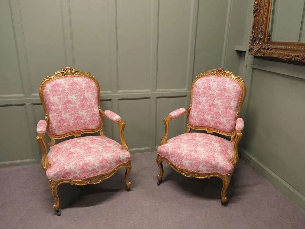 A pair of 19th-century French giltwood salon armchairs featuring carved floral frames and pink pattern fabric upholstery.