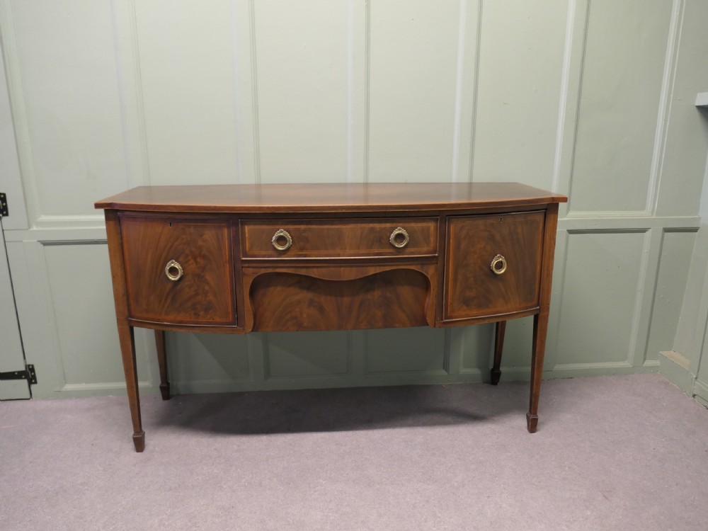 A Regency flame mahogany bowfront sideboard featuring inlaid stringing, a central drawer, two side cupboards, and tapered square legs with brass ring handles.