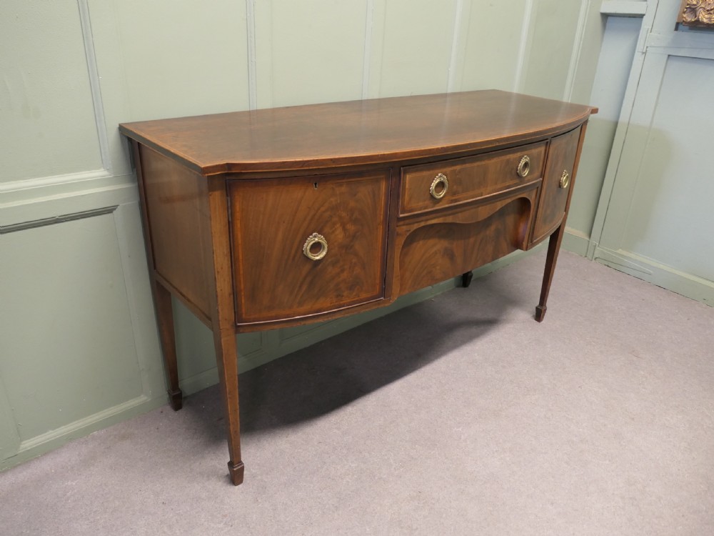A Regency flame mahogany bowfront sideboard featuring inlaid stringing, a central drawer, two side cupboards, and tapered square legs with brass ring handles. View III