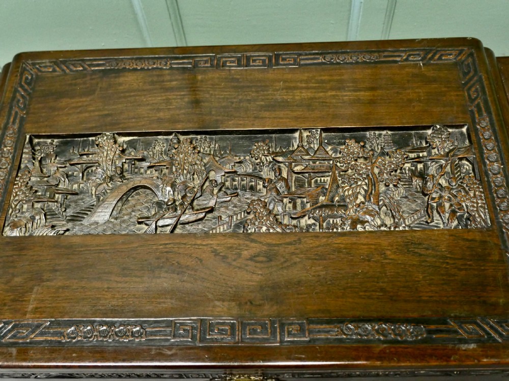 A dark brown carved camphor wood chest featuring detailed relief-carved architectural panels, a stepped Art Deco profile, and a brass latch plate. View II
