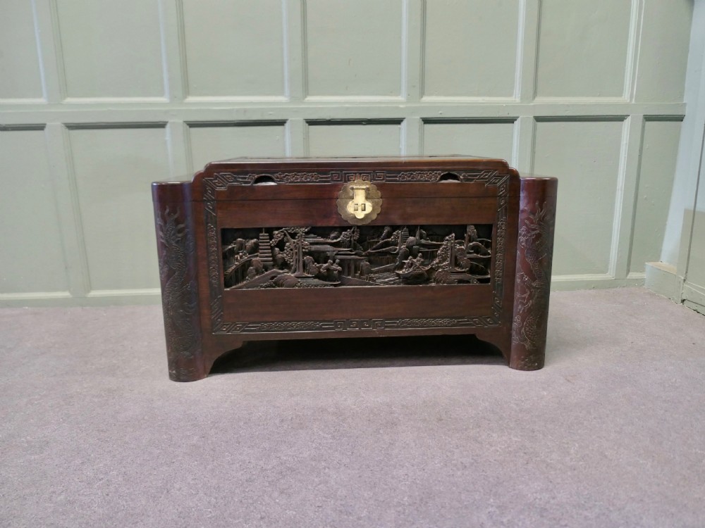 A dark brown carved camphor wood chest featuring detailed relief-carved architectural panels, a stepped Art Deco profile, and a brass latch plate. View IV