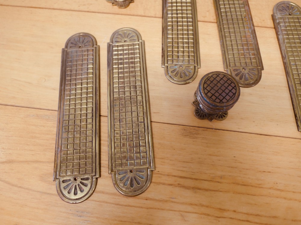 A set of brass Arts and Crafts finger plates and matching round door knobs featuring geometric lattice engraving and fan details. View II