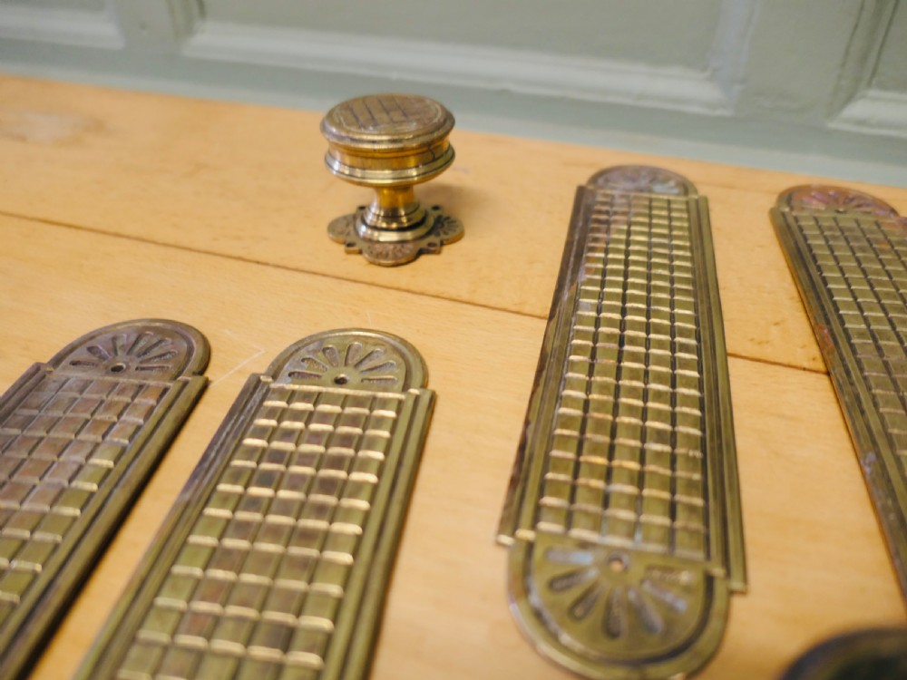 A set of brass Arts and Crafts finger plates and matching round door knobs featuring geometric lattice engraving and fan details. View V