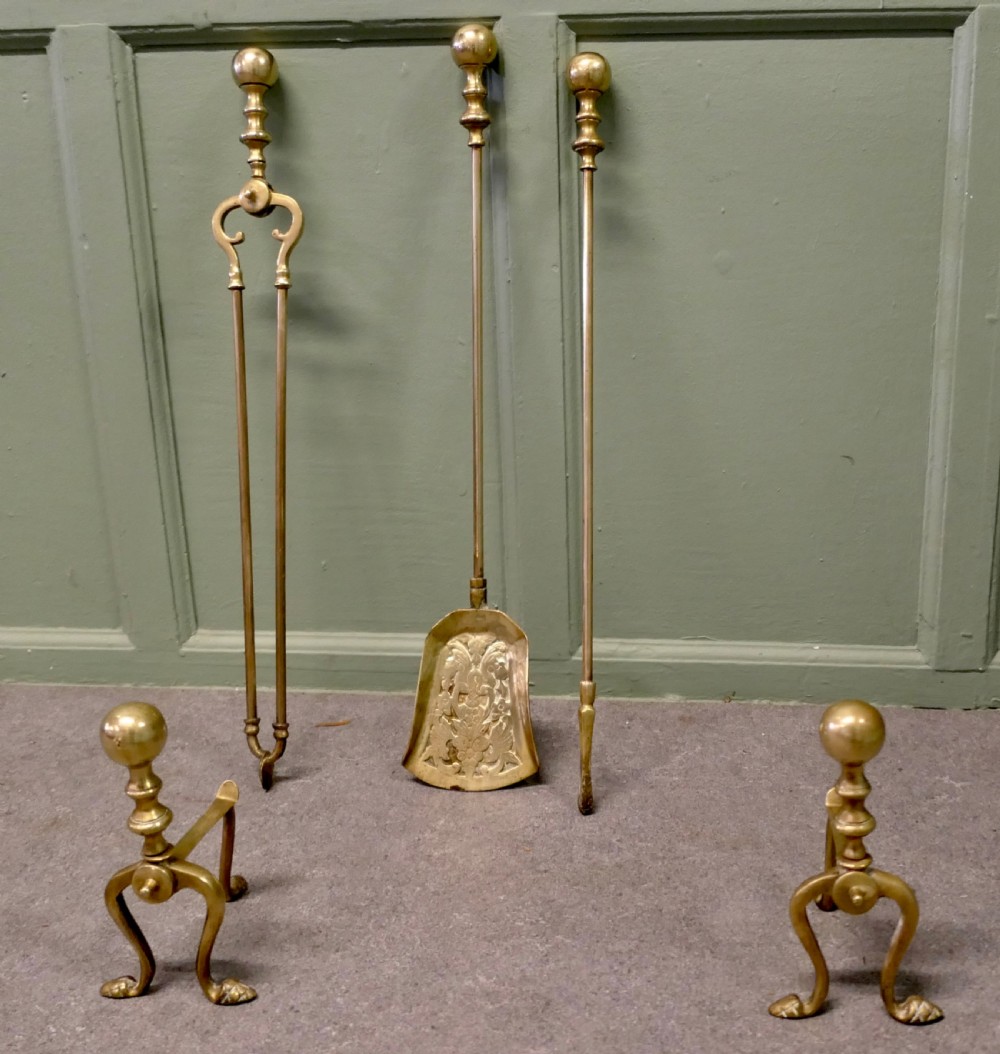 A solid brass fireplace tool set including a shovel, tongs, and poker resting horizontally on matching brass rests. View IV