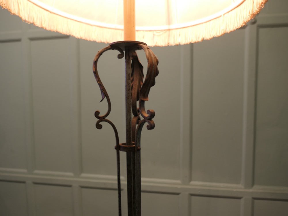 A tall wrought iron floor lamp featuring decorative scrollwork at the stem and base, finished with a cream fabric fringed shade. View V