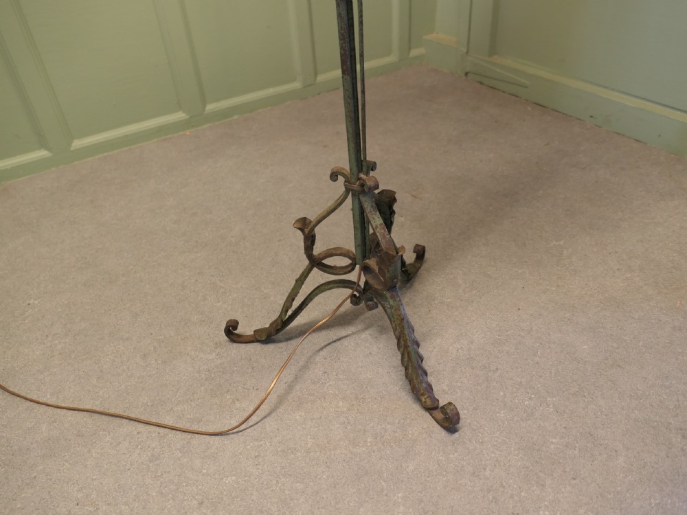 A tall wrought iron floor lamp featuring decorative scrollwork at the stem and base, finished with a cream fabric fringed shade. View VI