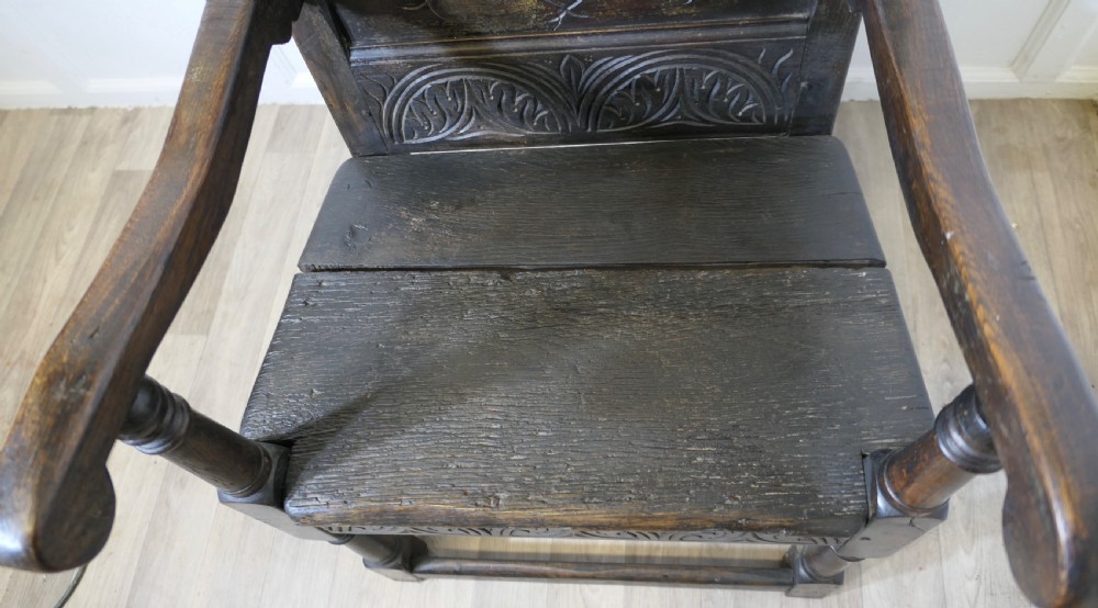 An 18th-century carved dark oak wainscot armchair featuring a detailed geometric back panel, turned supports, and a flat wooden seat. View VII