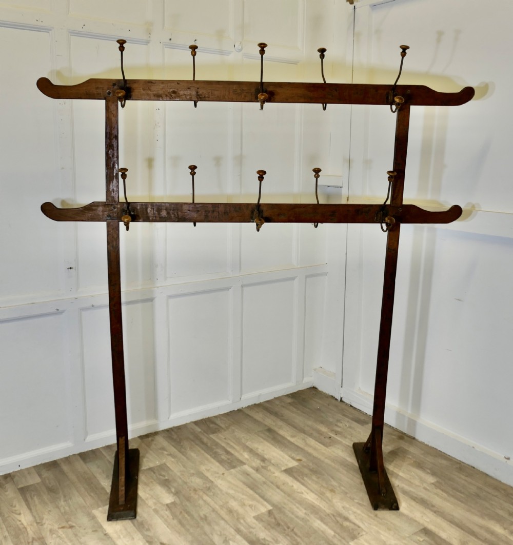 A freestanding double-sided French Arts and Crafts coat rack crafted from golden pine with two horizontal bars holding metal and wood pegs.