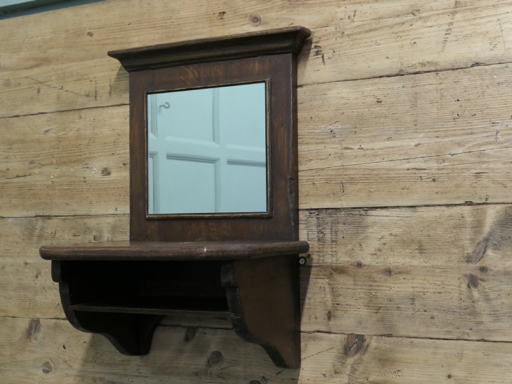 A dark oak wall-mounted mirror featuring a square glass panel surrounded by a moulded wood frame above an integrated display shelf with shaped support brackets. View II