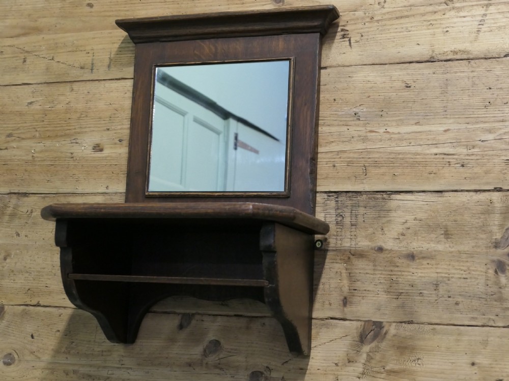 A dark oak wall-mounted mirror featuring a square glass panel surrounded by a moulded wood frame above an integrated display shelf with shaped support brackets. View III