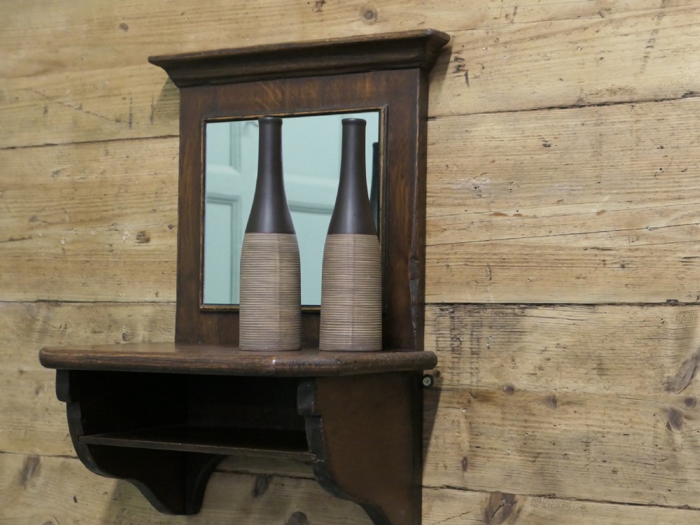 A dark oak wall-mounted mirror featuring a square glass panel surrounded by a moulded wood frame above an integrated display shelf with shaped support brackets. View V