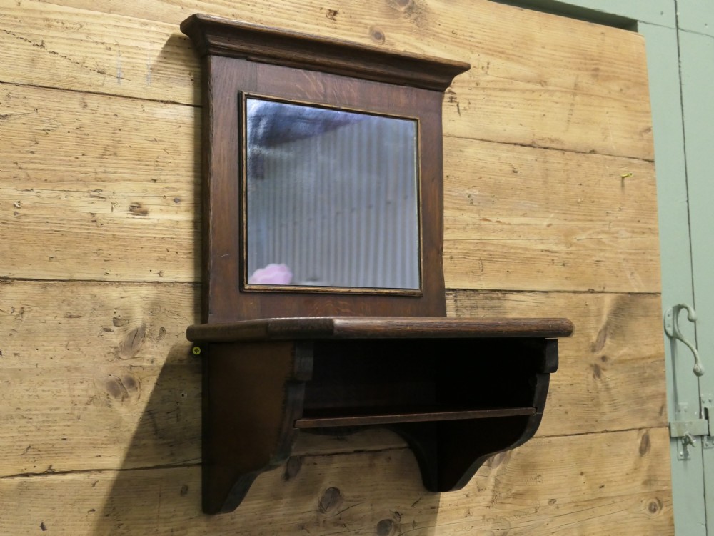 A dark oak wall-mounted mirror featuring a square glass panel surrounded by a moulded wood frame above an integrated display shelf with shaped support brackets. View VI