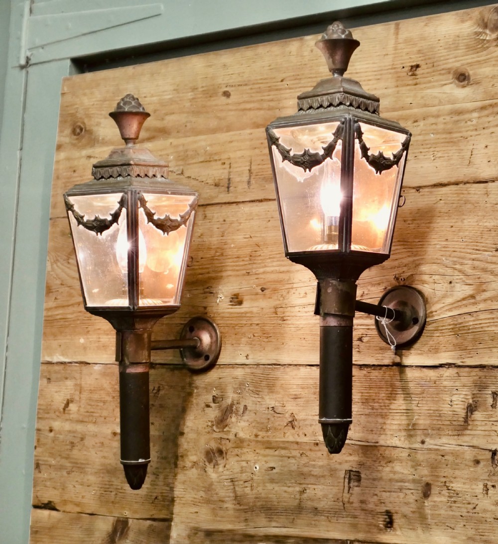 A pair of French Empire style aged brass carriage lanterns with glass panels, leaf swags, and urn finials mounted on cylindrical stems.