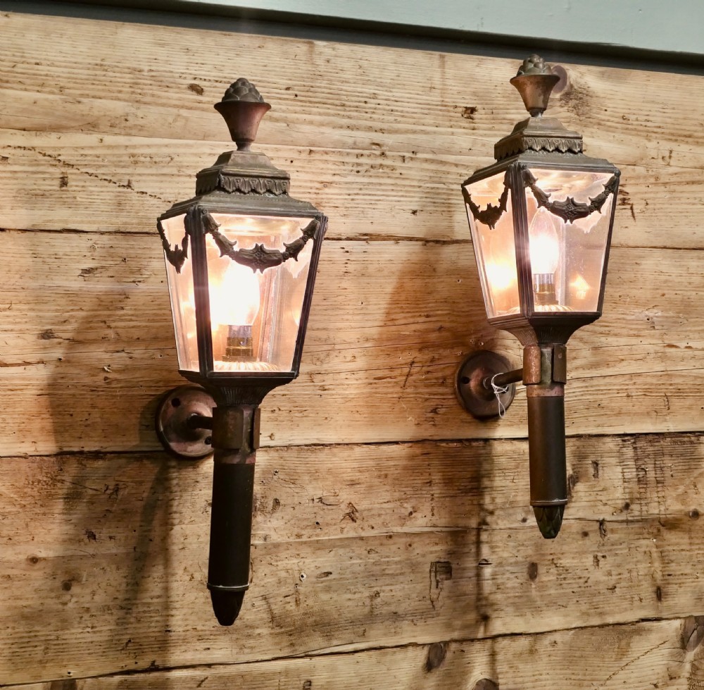 A pair of French Empire style aged brass carriage lanterns with glass panels, leaf swags, and urn finials mounted on cylindrical stems. View III
