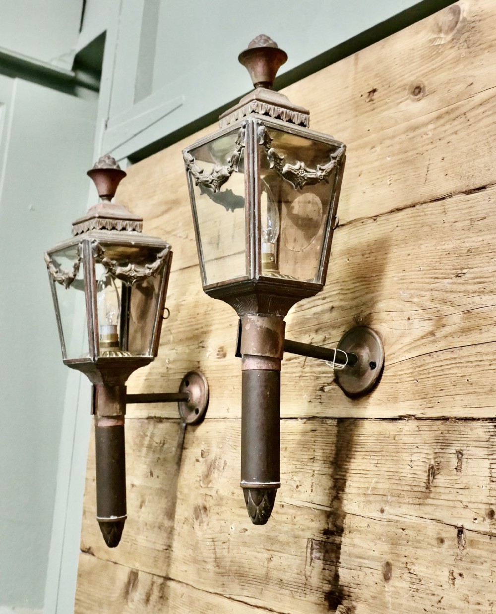 A pair of French Empire style aged brass carriage lanterns with glass panels, leaf swags, and urn finials mounted on cylindrical stems. View IV