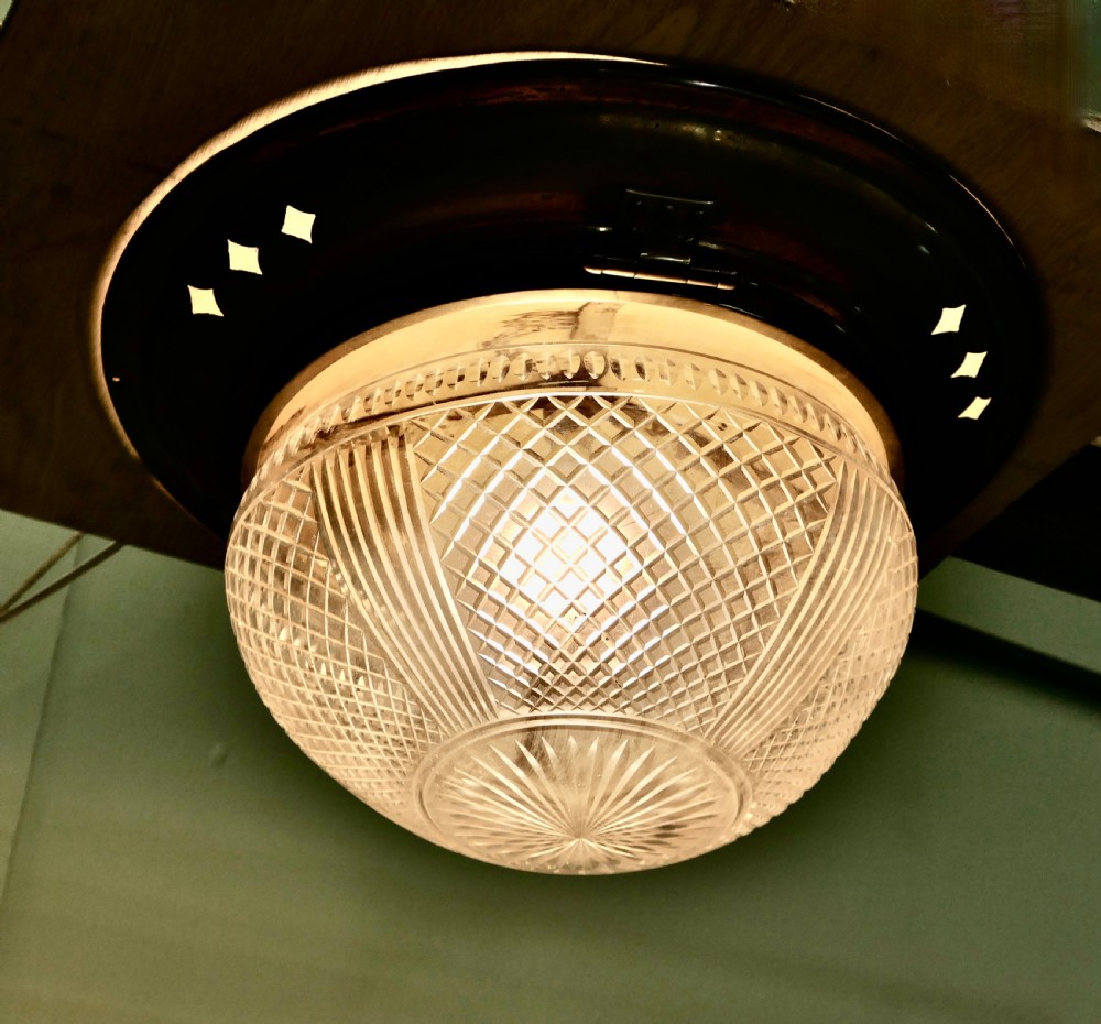 An Art Deco flush mount ceiling light featuring a hemispherical cut glass shade with geometric diamond patterns set into a dark metal collar with diamond-shaped perforations.