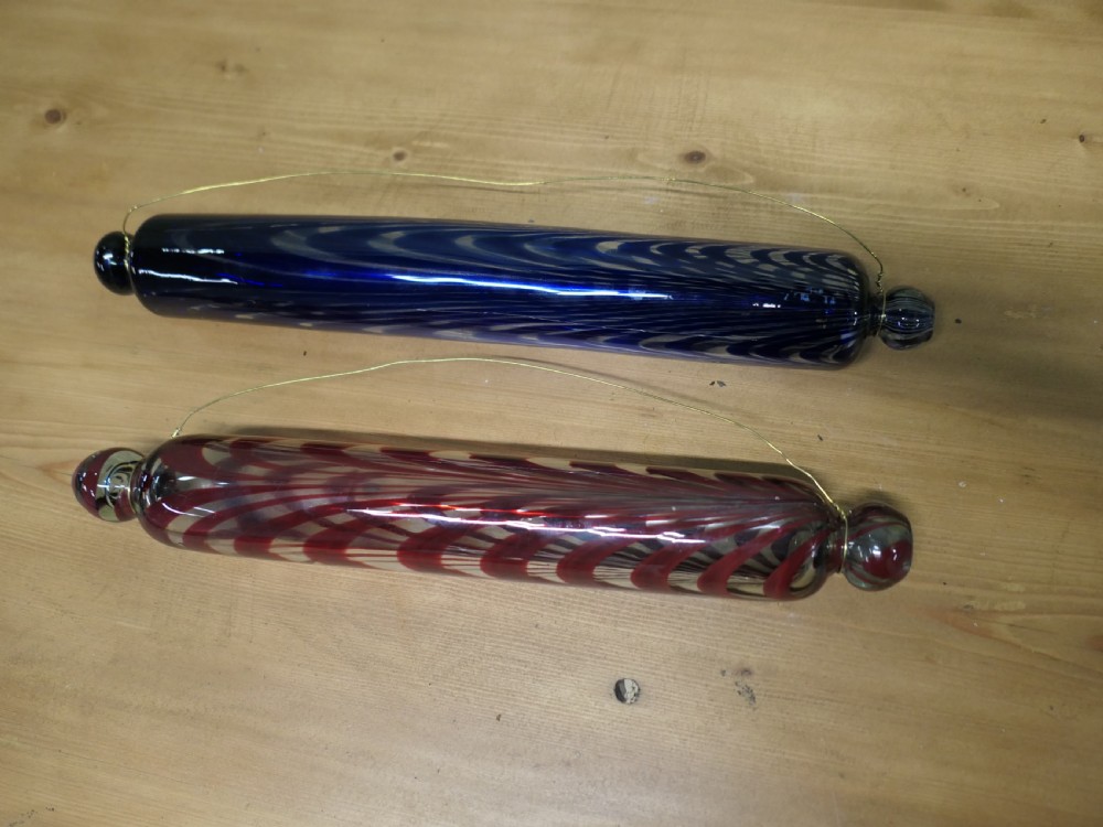 A pair of 19th-century hand-blown glass rolling pins featuring swirled trailing patterns in cobalt blue and ruby red.