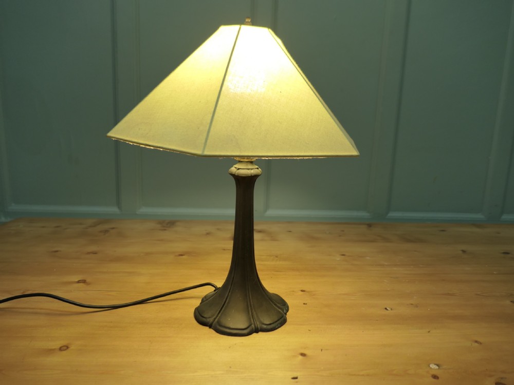 An Art Nouveau table lamp featuring a flared dark metal spelter base and a cream pyramidal fabric shade.