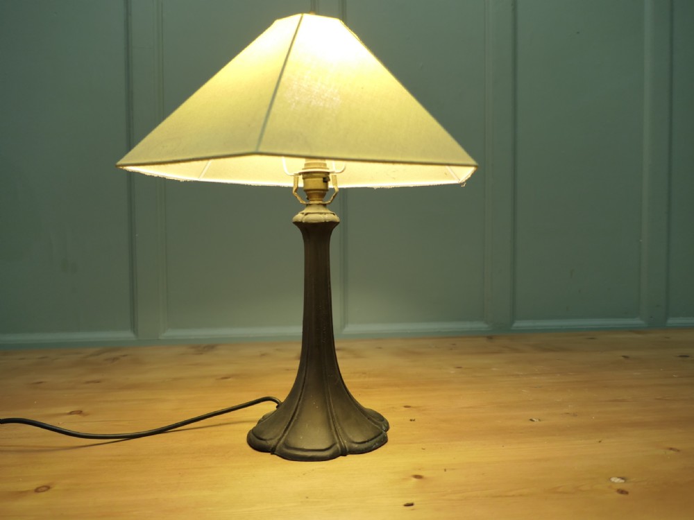 An Art Nouveau table lamp featuring a flared dark metal spelter base and a cream pyramidal fabric shade. View III