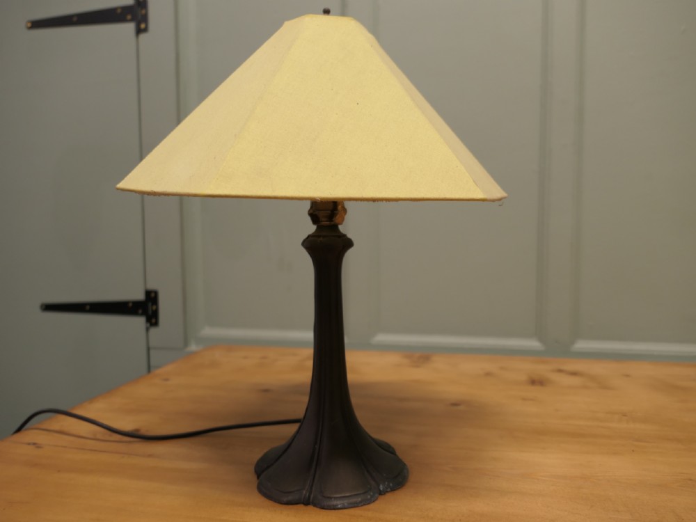 An Art Nouveau table lamp featuring a flared dark metal spelter base and a cream pyramidal fabric shade. View V